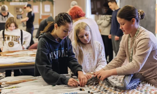 Young women weave a mat out of plastic as part of a service project.