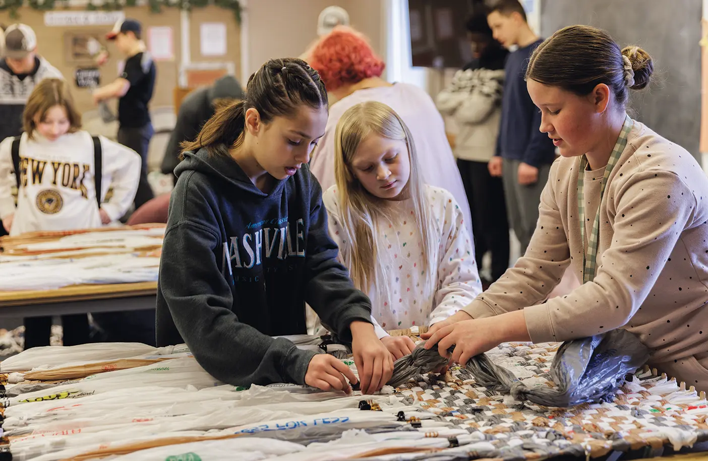 Young women weave a mat out of plastic as part of a service project.