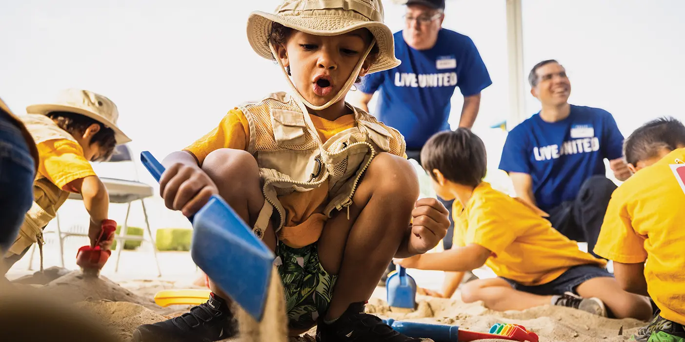 Children digging in a sandbox for toy dinosaurs, supervised by BYU employees.
