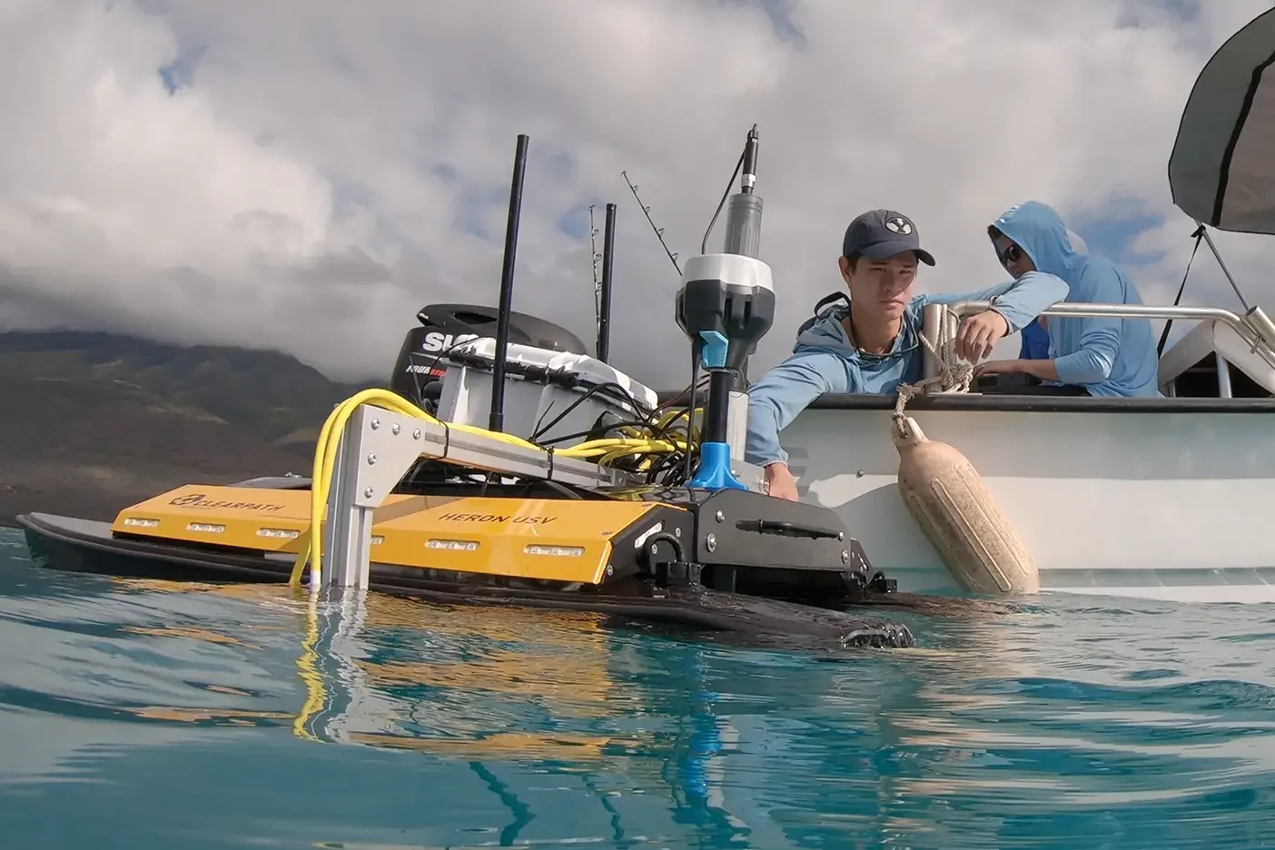 A BYU graduate student in a boat works holds a aquatic drone beside the boat.