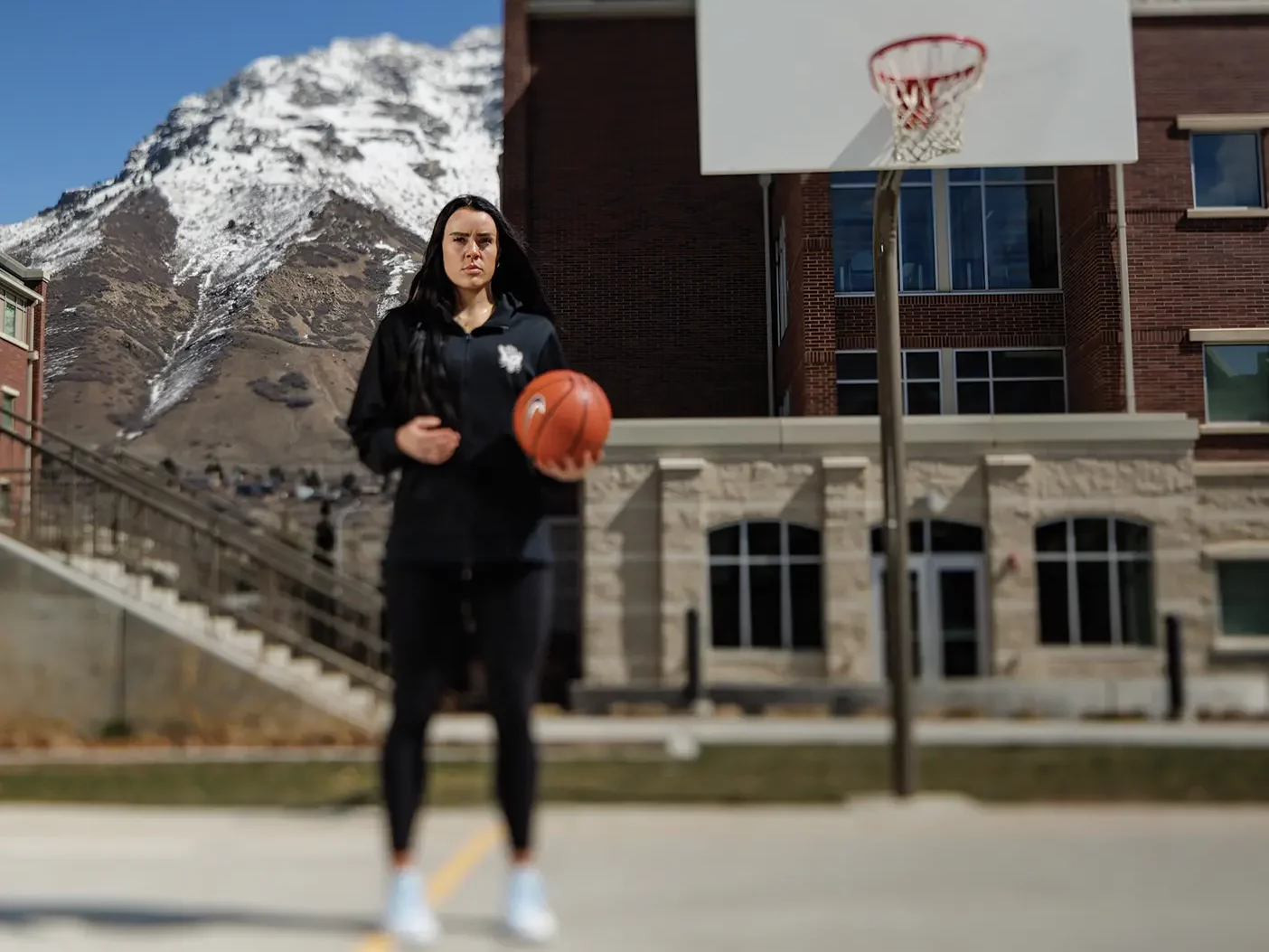 Lauren Gustin poses with a basketball in one hand on an outdoor court.