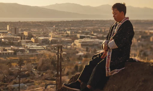 Yang Vang sits on a sun-bathed slope overlooking BYU's campus, wearing traditionall Hmong clothing.