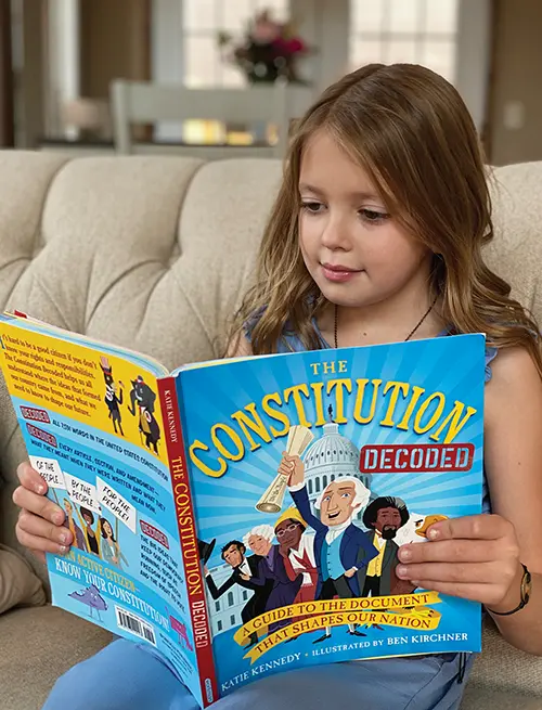 A young girl reads a picture book called "The Constitution Decoded."