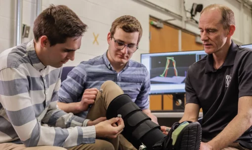 Three men in an engineering lab examine a medical boot by placing nodes on it.