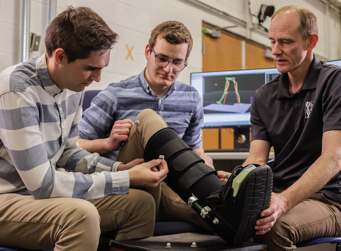 Three men in an engineering lab examine a medical boot by placing nodes on it.