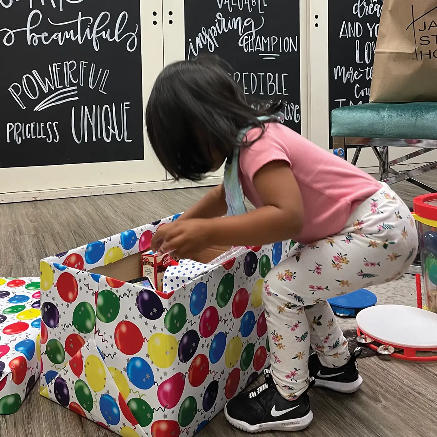 A child reaches into a box decorated with birthday balloons.