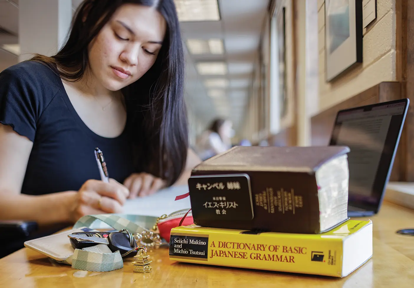 A female student studies in the Harold B. Lee Library. Her missionary name tag is on a pair of scriptures and a Japanese language book is out.