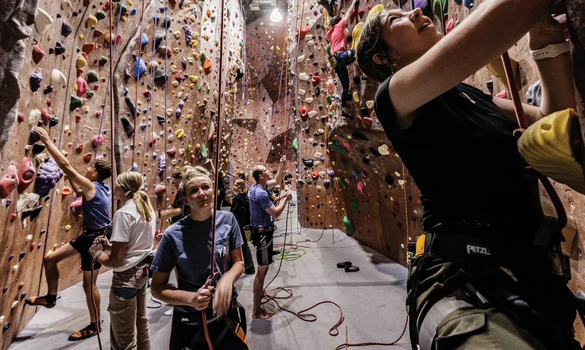 A BYU student looks up at the rock climbing wall in an indoor venue.