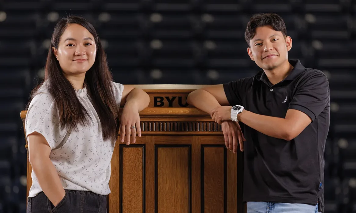 Two BYU Speeches translations students, a man and a woman, pose by a podium in the Marriott Center.