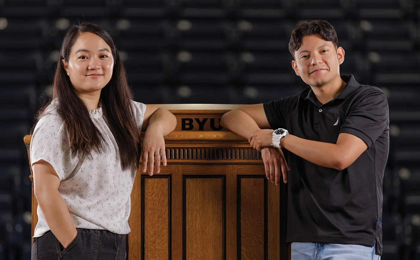 Two BYU Speeches translations students, a man and a woman, pose by a podium in the Marriott Center.