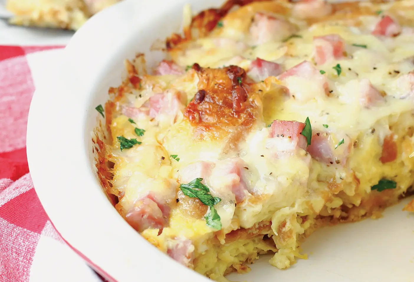 A combination of ham, cheese, eggs, and other ingredients sits freshly baked in a white bowl, cut in half.