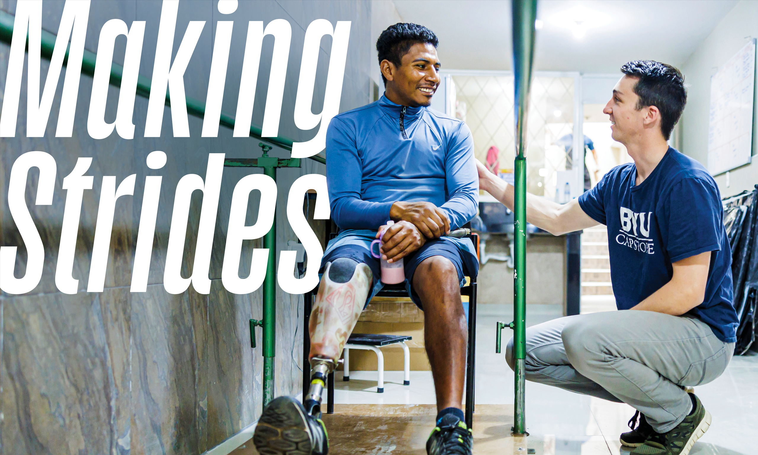 A man with a prosthetic leg sits in a wheelchair while smiling and talking to a BYU student.