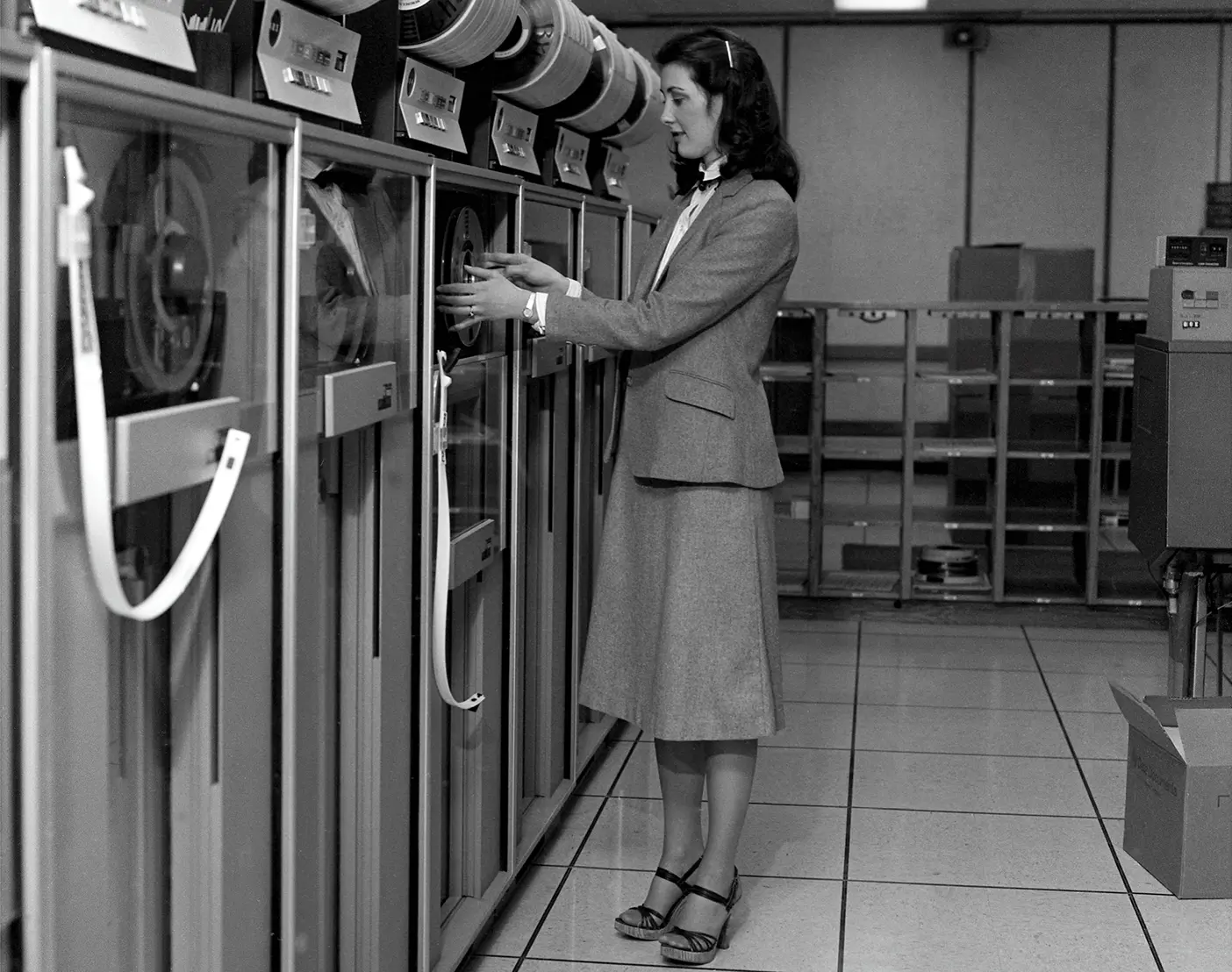 Woman dressed in long skirt and blazer adjusting large computer.