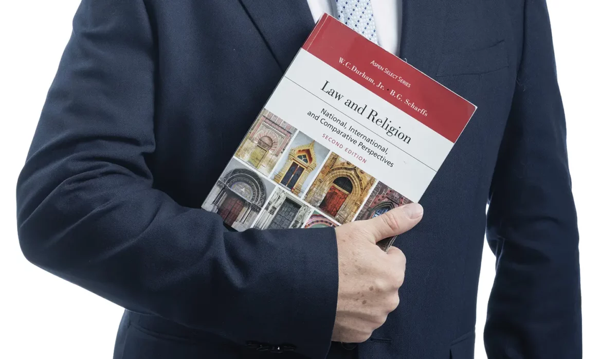 A male law professor in a suit and tie holds a textbook about law and religious liberty