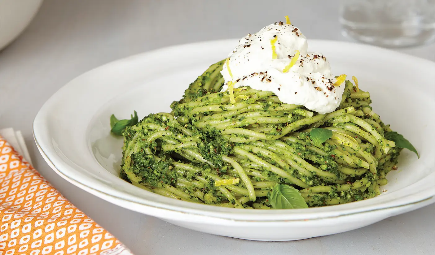 A plate of green pesto pasta with lemon ricotta cream.