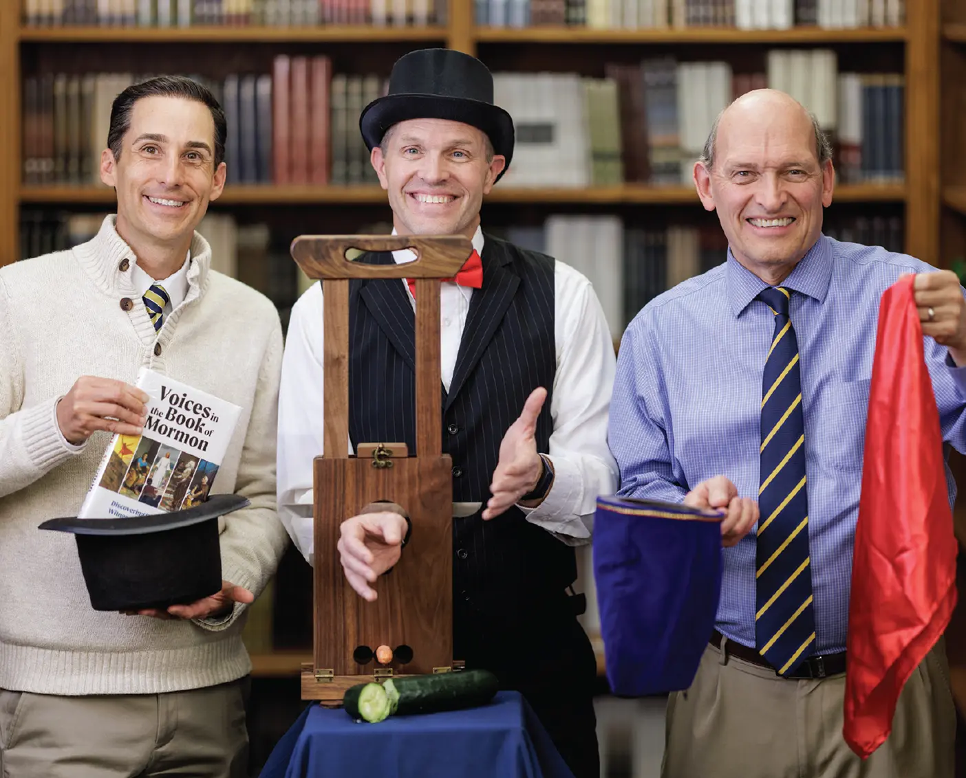 John Hilton III pulls his book "Voices in the Book of Mormon" from a hat, Devan Jensen demonstrates a guillotine magic trick, and Alex Baugh holds other magic props.   
