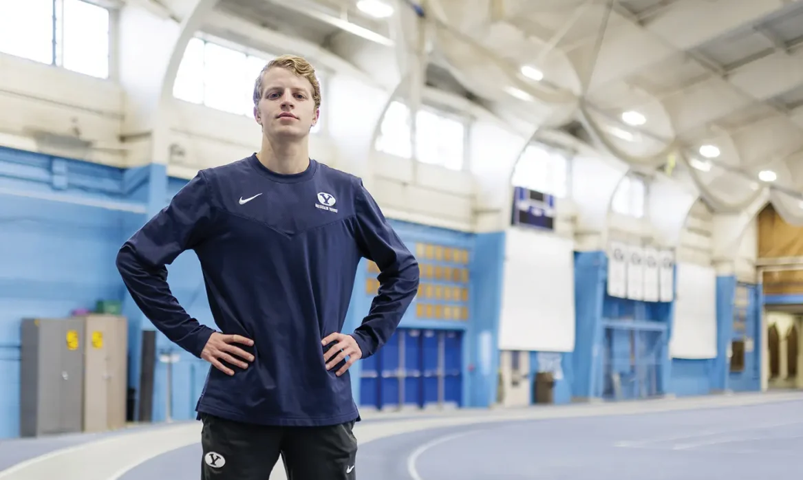Aidan Troutner stands on the track indoors with hands on hips, looking triumphantly at the camera.