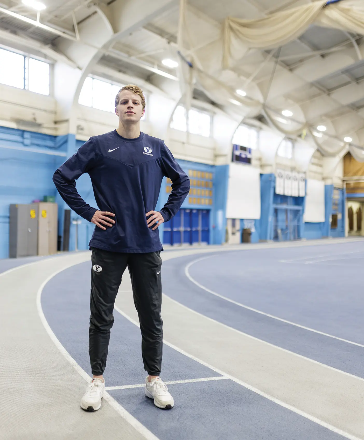 Aidan Troutner stands on the track indoors with hands on hips, looking triumphantly at the camera.