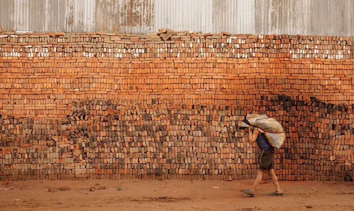 A wall of bricks with a bricklayer carrying a sack.