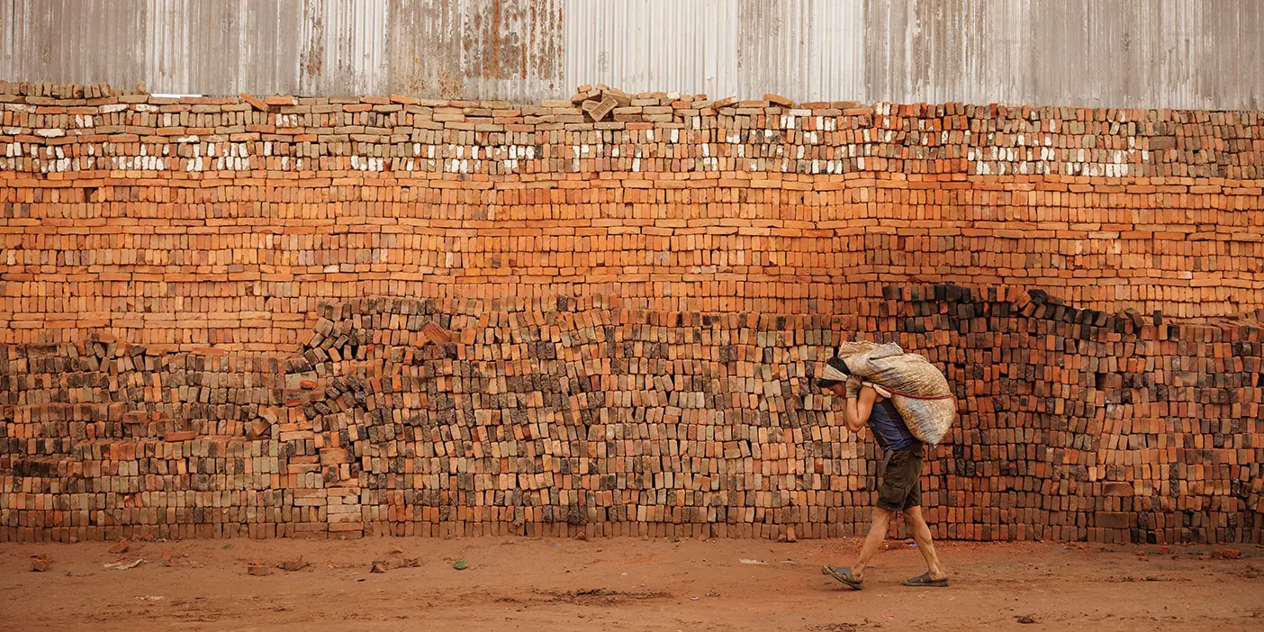 A wall of bricks with a bricklayer carrying a sack.