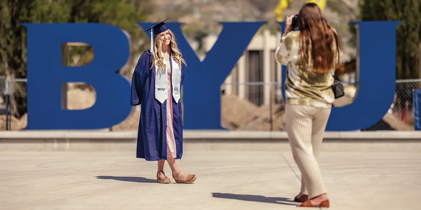 A BYU grad poses in front of a BYU-themed photo-op.