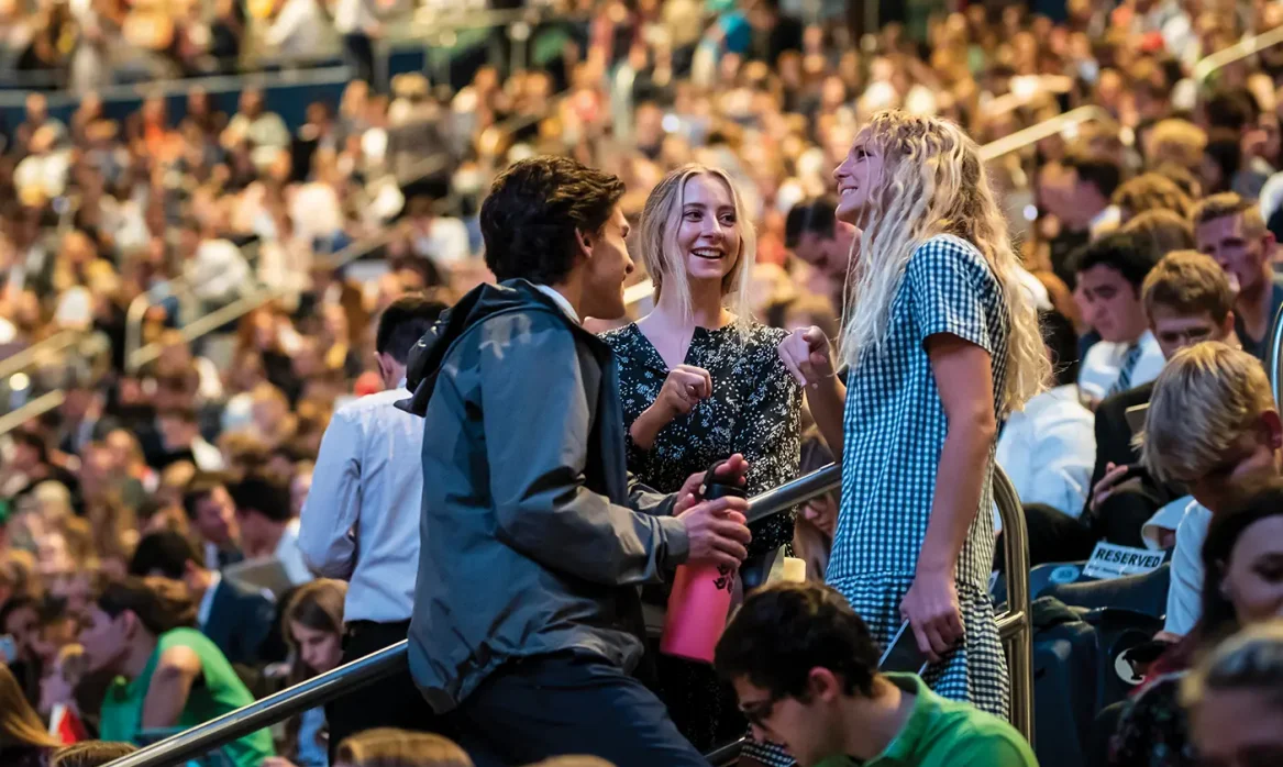 Three college students stand up and talk at a BYU devotional.