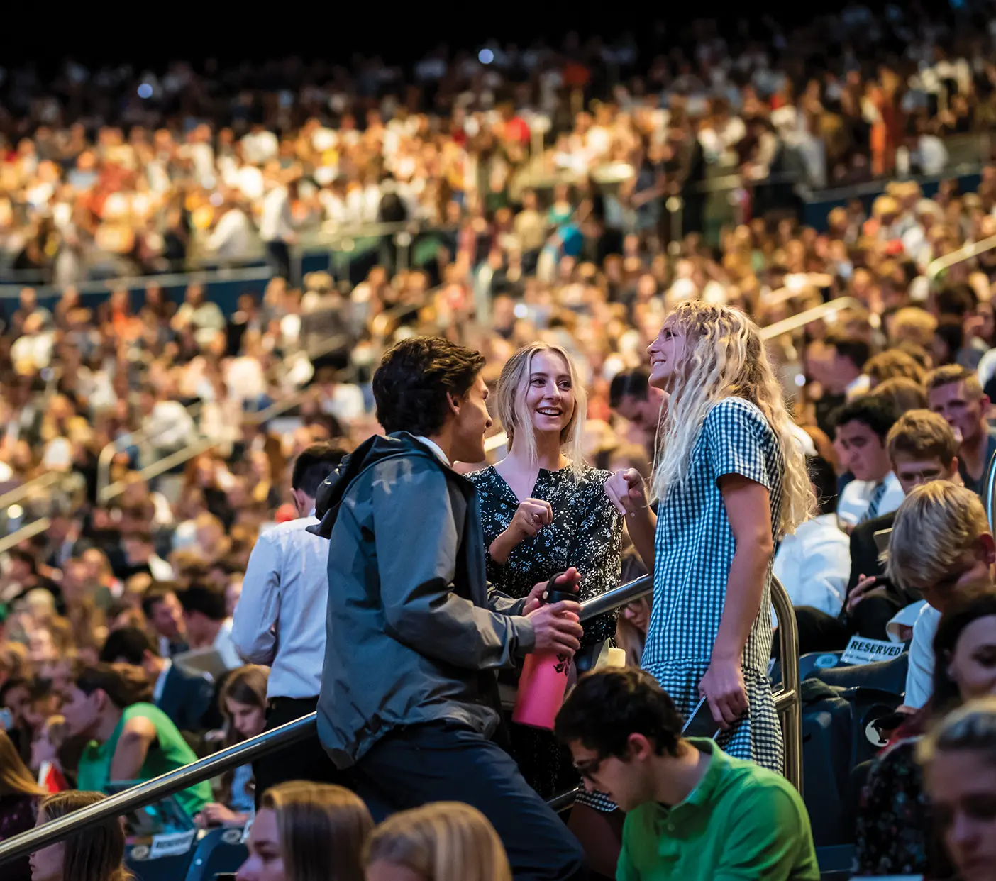 Three college students stand up and talk at a BYU devotional.