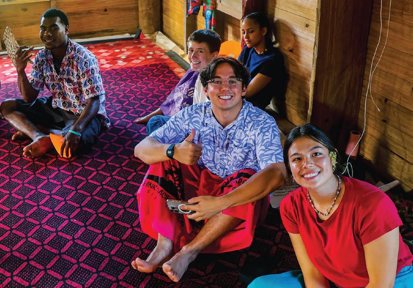 BYU students Zachary Napierski (center) and Mia Okhi sit in a Fiji dwelling during an international experience.