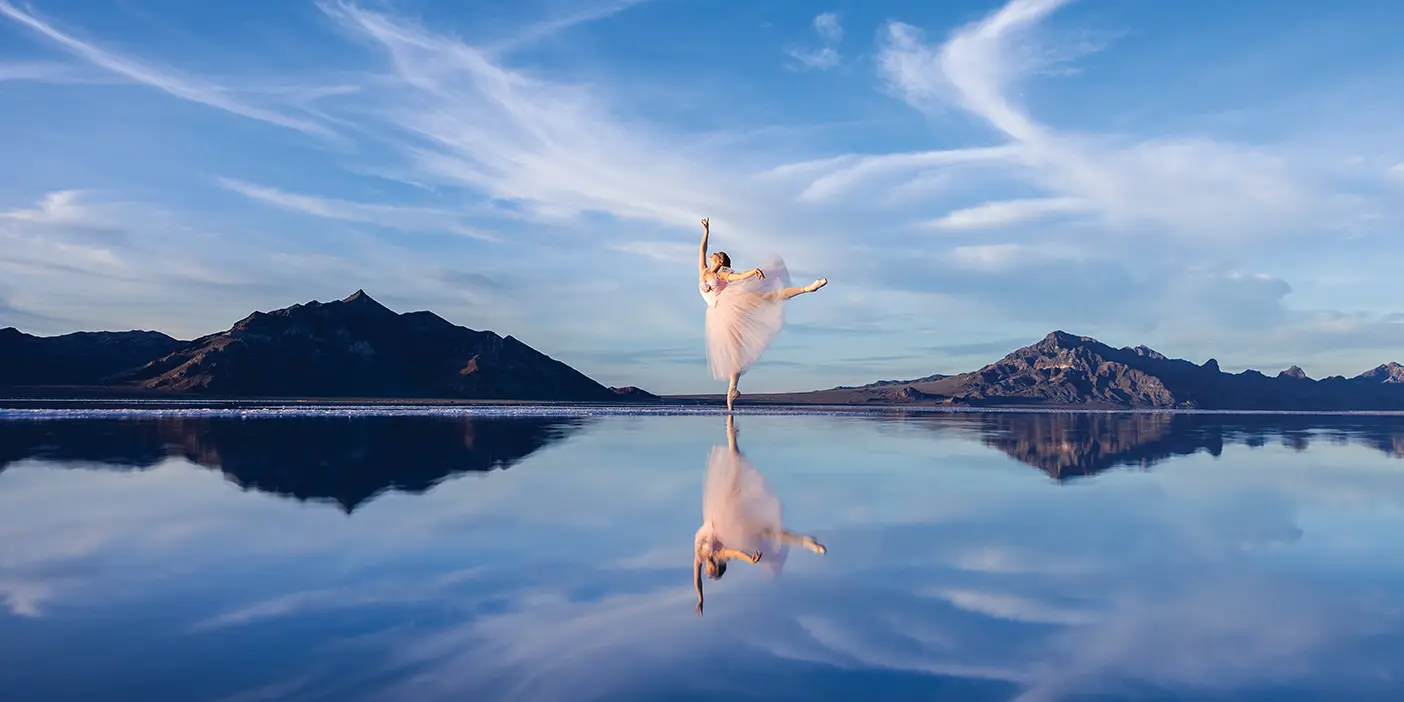 Brooklyn Jarvis Kelson's photo of a dancer in pink poses at the Salt Flats with mountains behind her. Because of the reflective water beneath her, it looks she is floating between the earth and the sky.