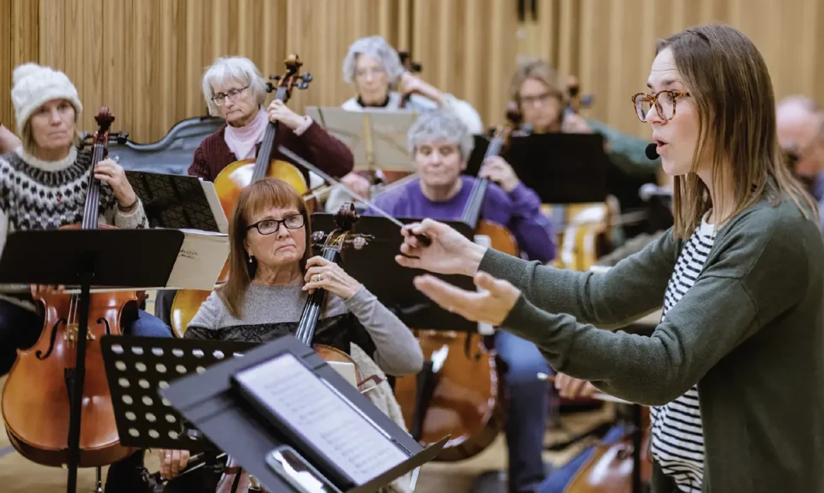 A woman conducts a string orchestra made up of older adults