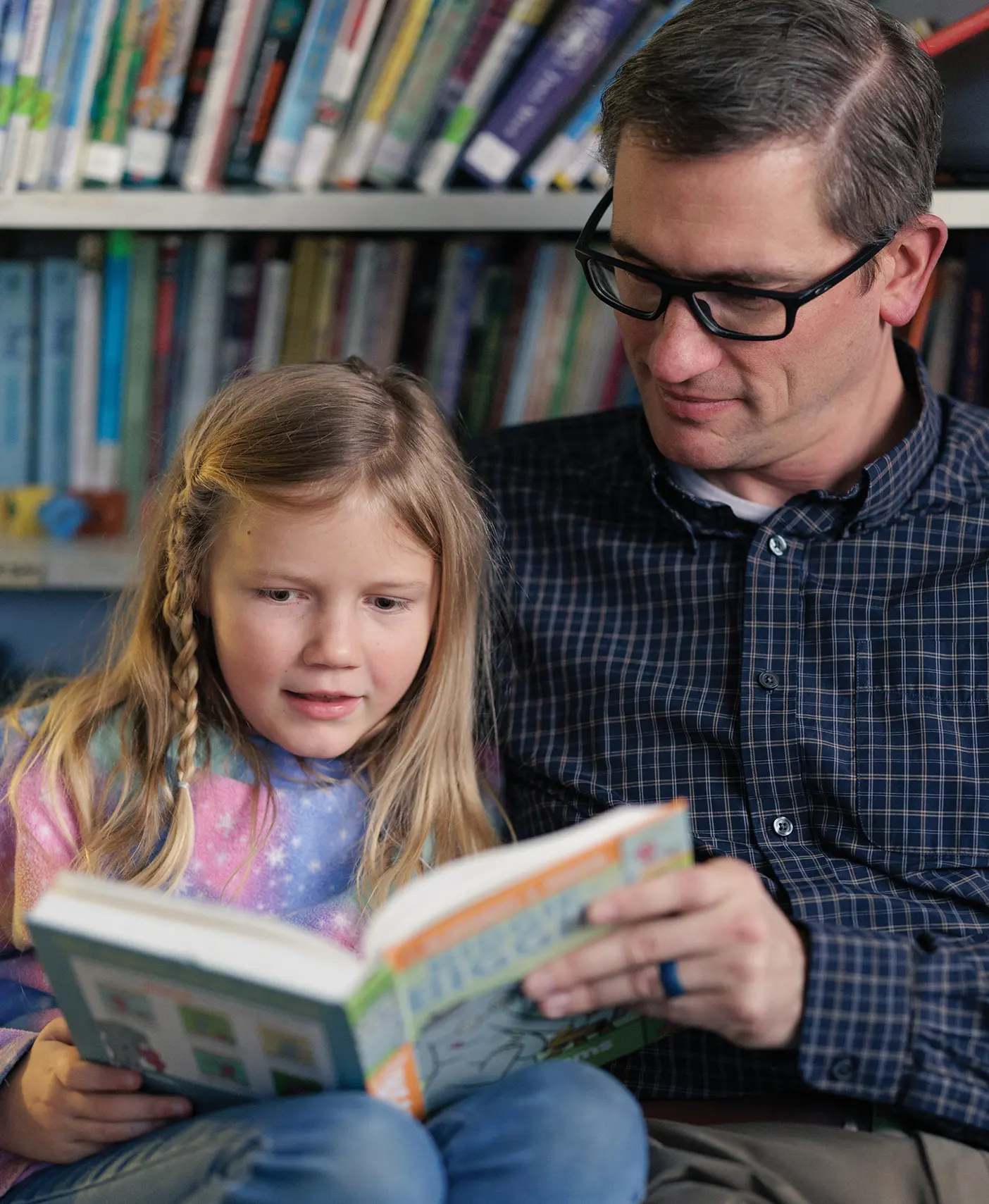 A father and young daughter enjoy reading a book together.