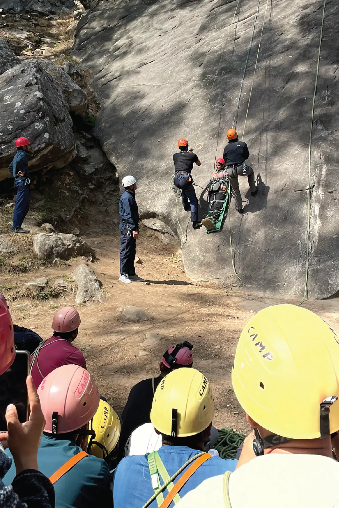 A few people on a rock face show onlookers how to rescue and treat injured mountain travelers.