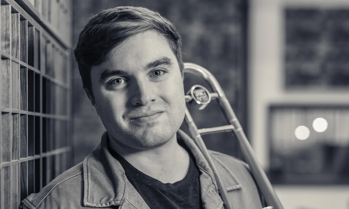 Commercial music student Kevin leans against a wall with a trombone