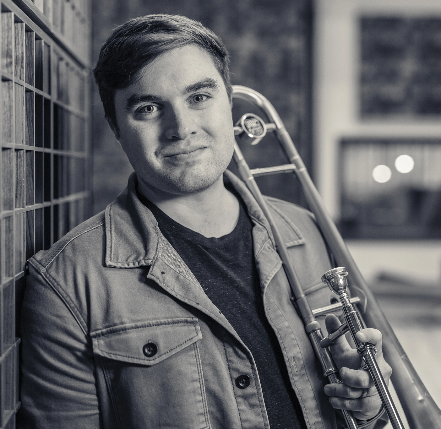 Commercial music student Kevin leans against the wall with a trombone.