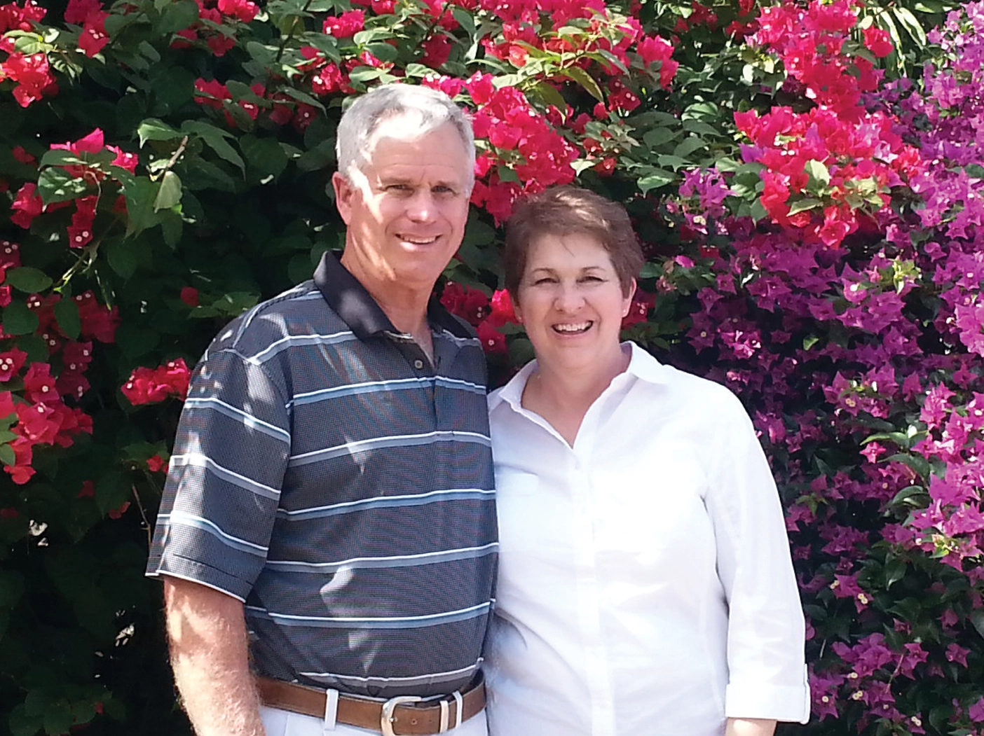 Butch and Debbie pose together in front of some bright flowers.