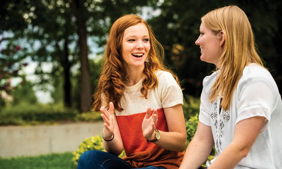 Two female students talk about Univ 101 while sitting outside on campus.