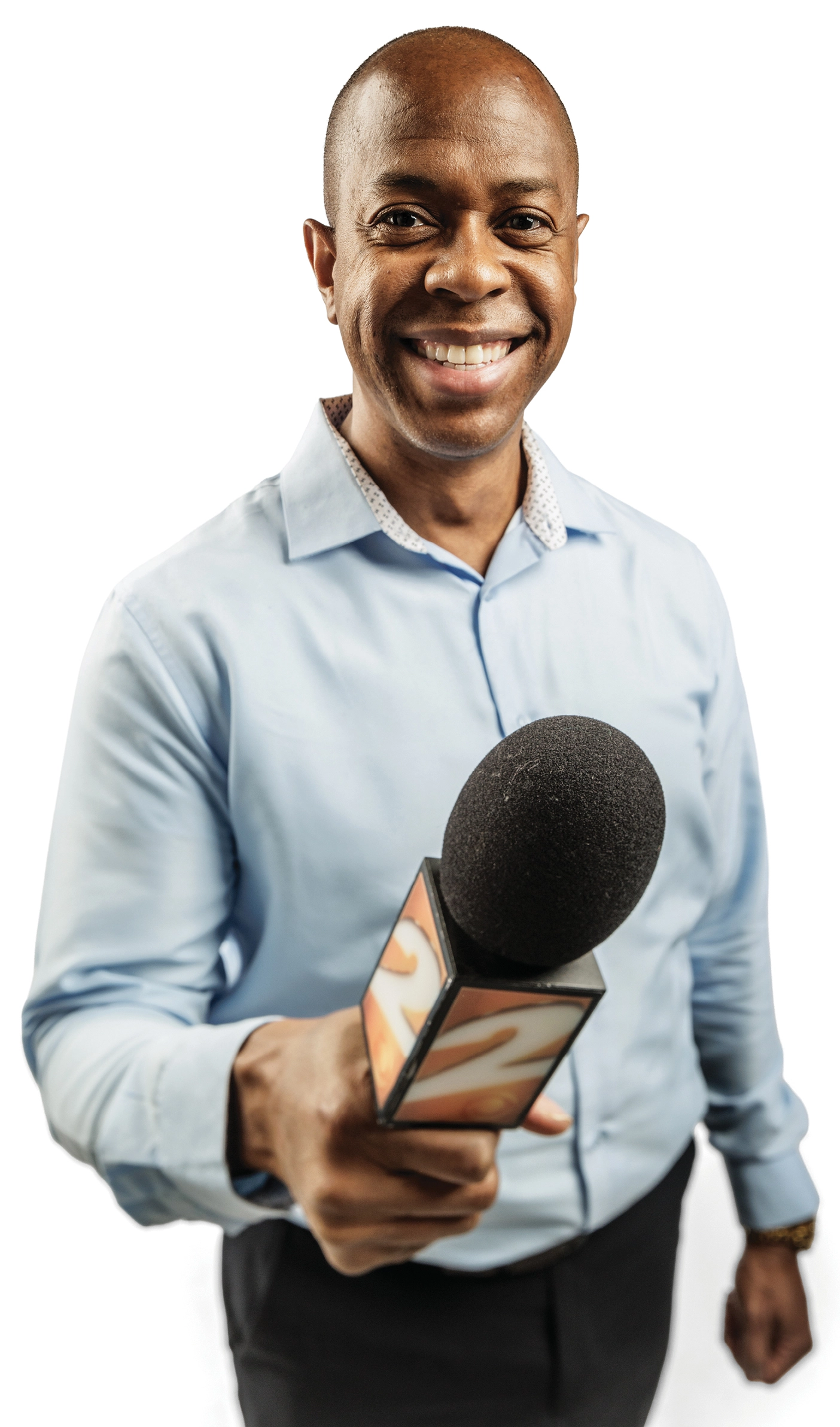 A smiling man in business attire points a microphone toward the viewer