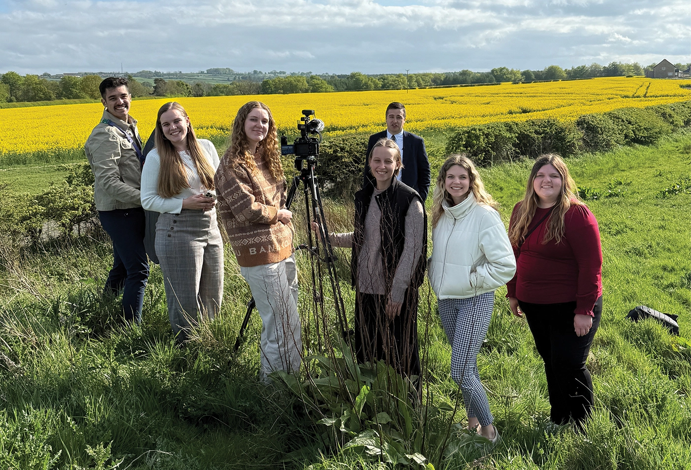 A group of BYU journalism students stand in a field with their camera filming their documentary 