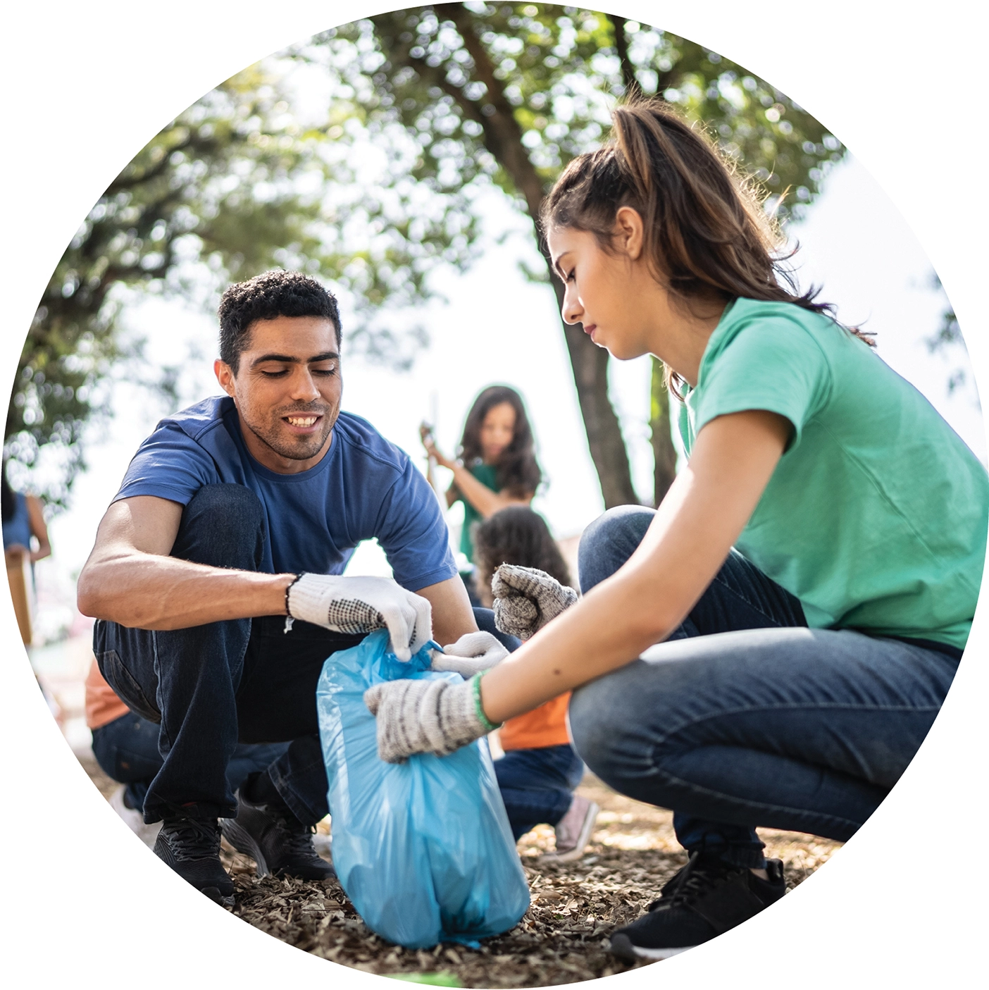 A girl wearing gardening gloves holds open a bag for a boy also wearing gardening gloves.