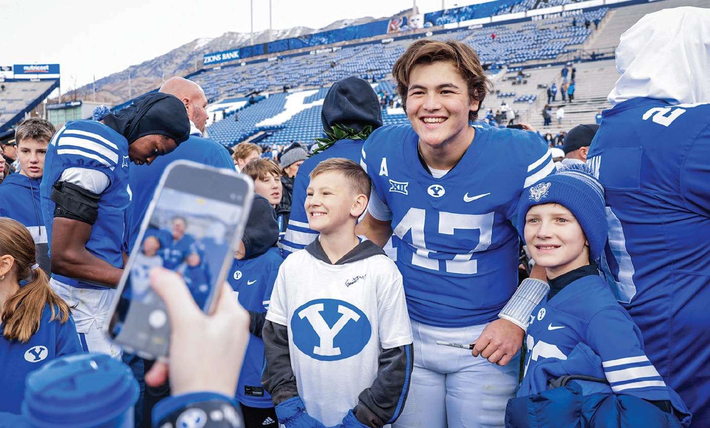 Bear Bachmeier poses for a photo on the field of Lavell Edwards Stadium in his jersey with two young fans.