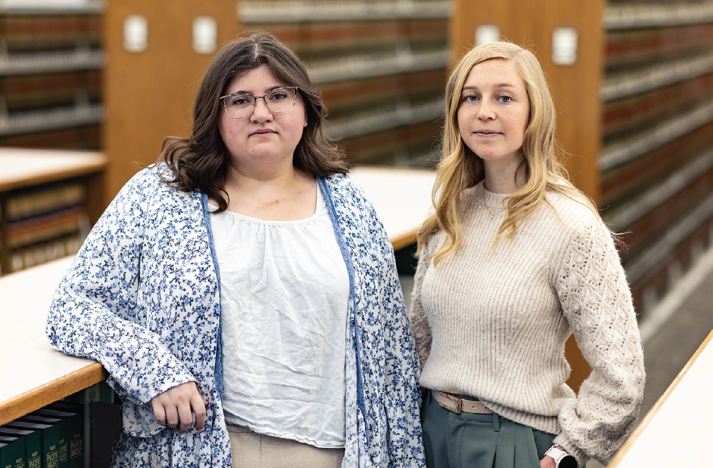 Graciana Messier and Isabelle Hasselt pose in front of a bookshelf in a library.