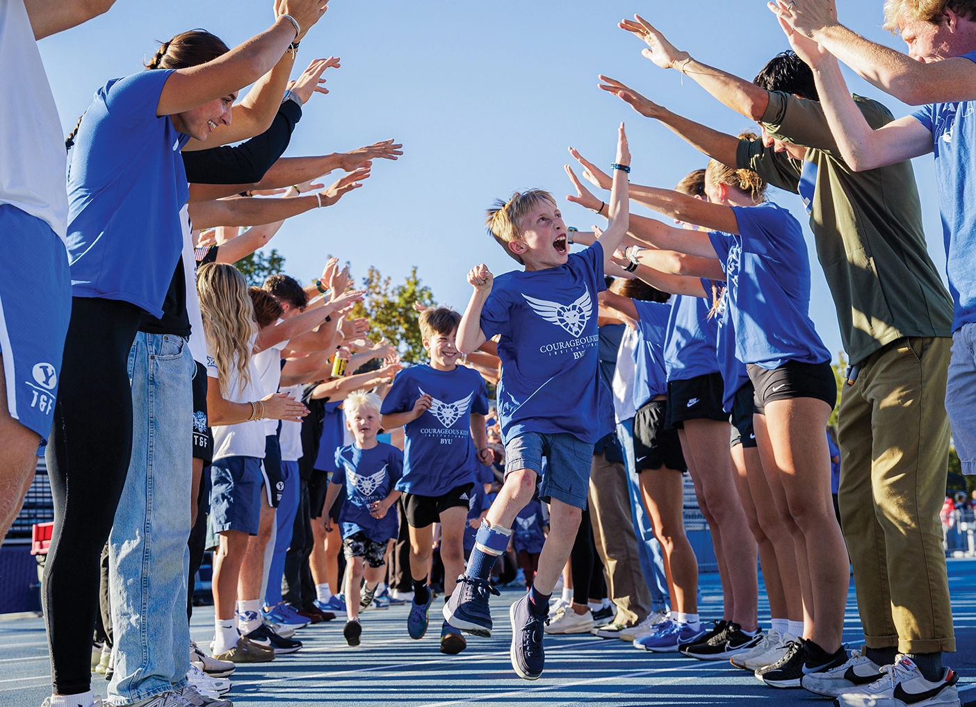 A boy running through a tunnel of people lined up and cheering jumps up for a high-five.
