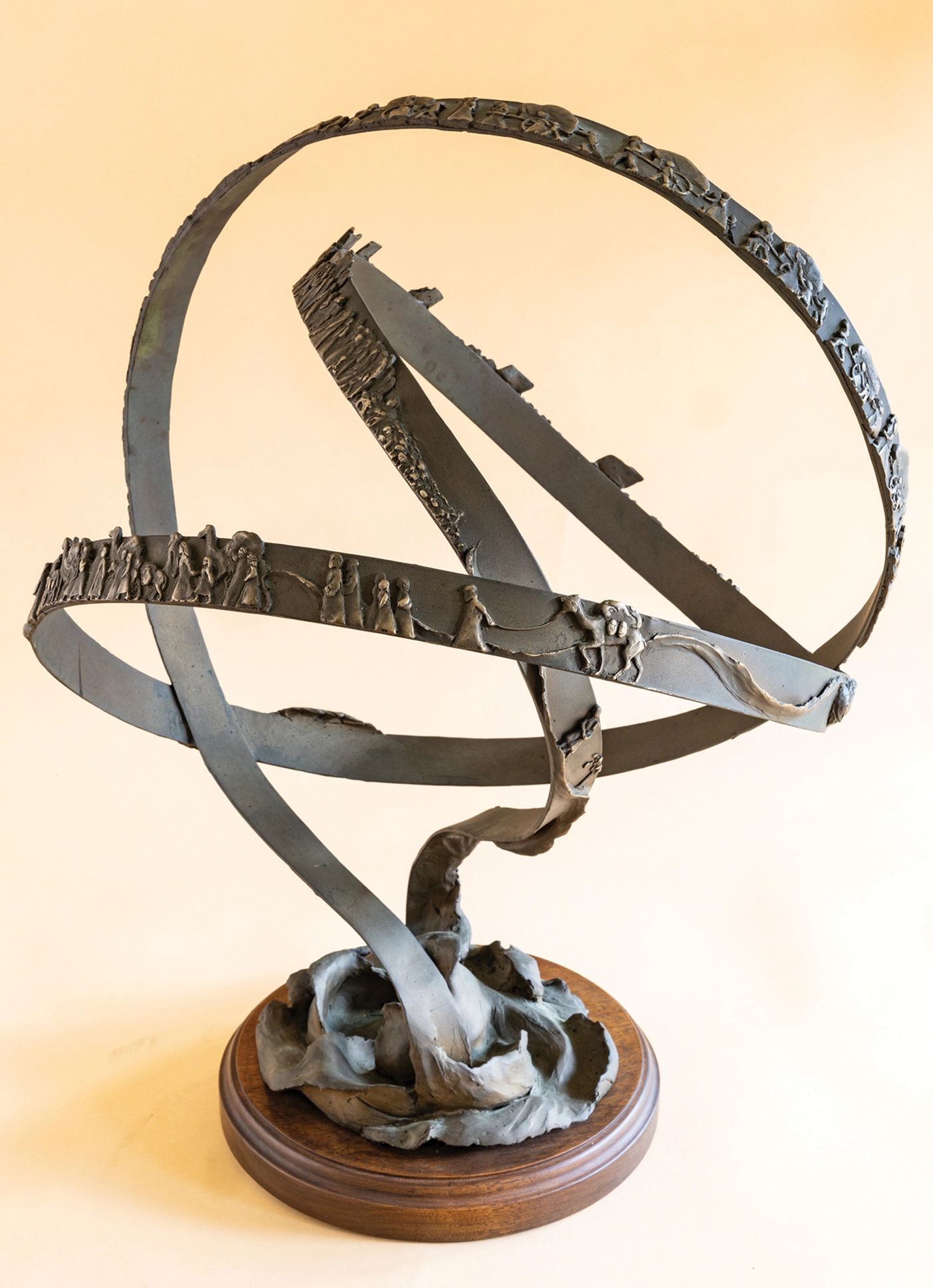 Round sculpture depicting figures on a metal ribbon. 