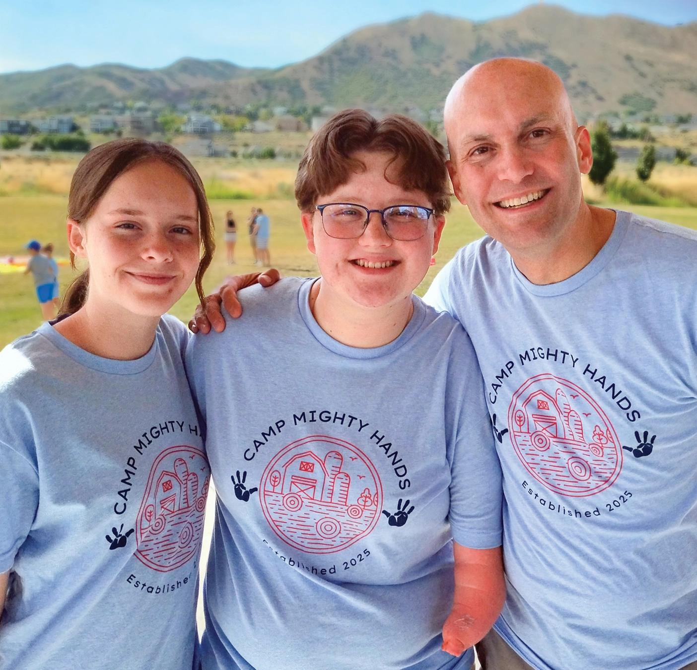 Andrew Bracken,, founder of Camp Mighty Hands, poses with two kids who have hand conditions in Camp Mighty Hands shirts.