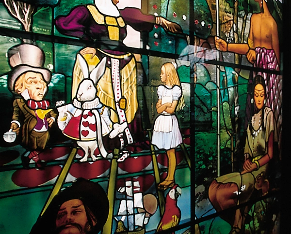 Close-up of a brightly colored stained-glass window depicting numerous storybook-like human and animal figures in small narrative scenes.
