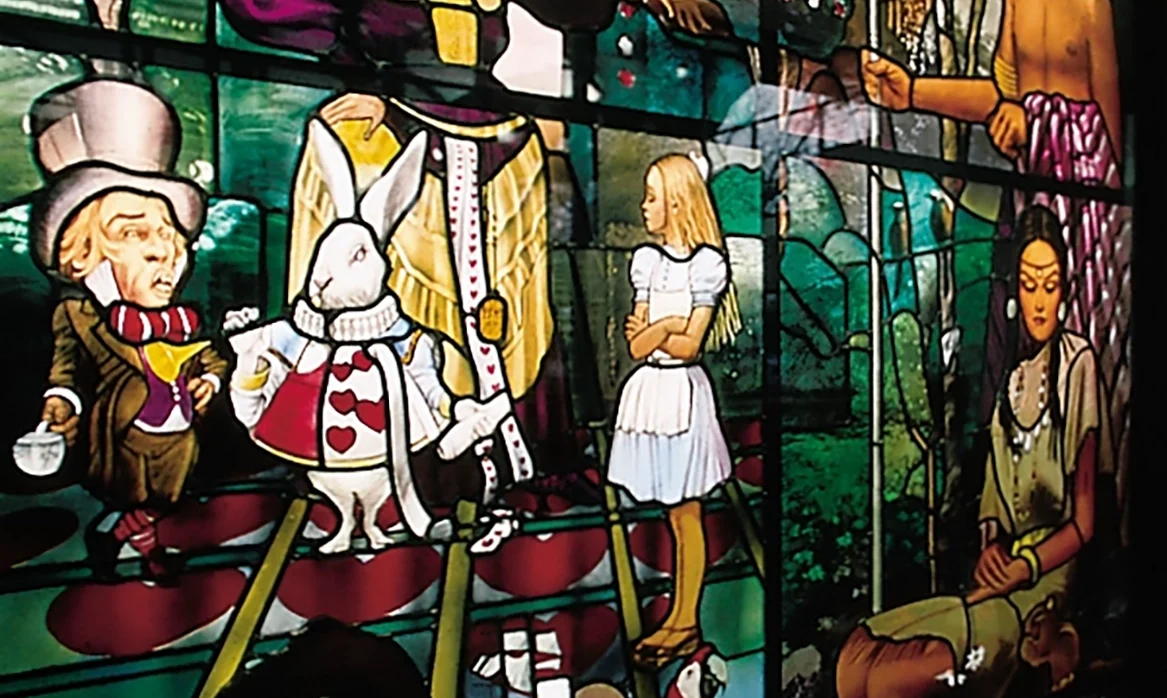 Close-up of a brightly colored stained-glass window depicting numerous storybook-like human and animal figures in small narrative scenes.