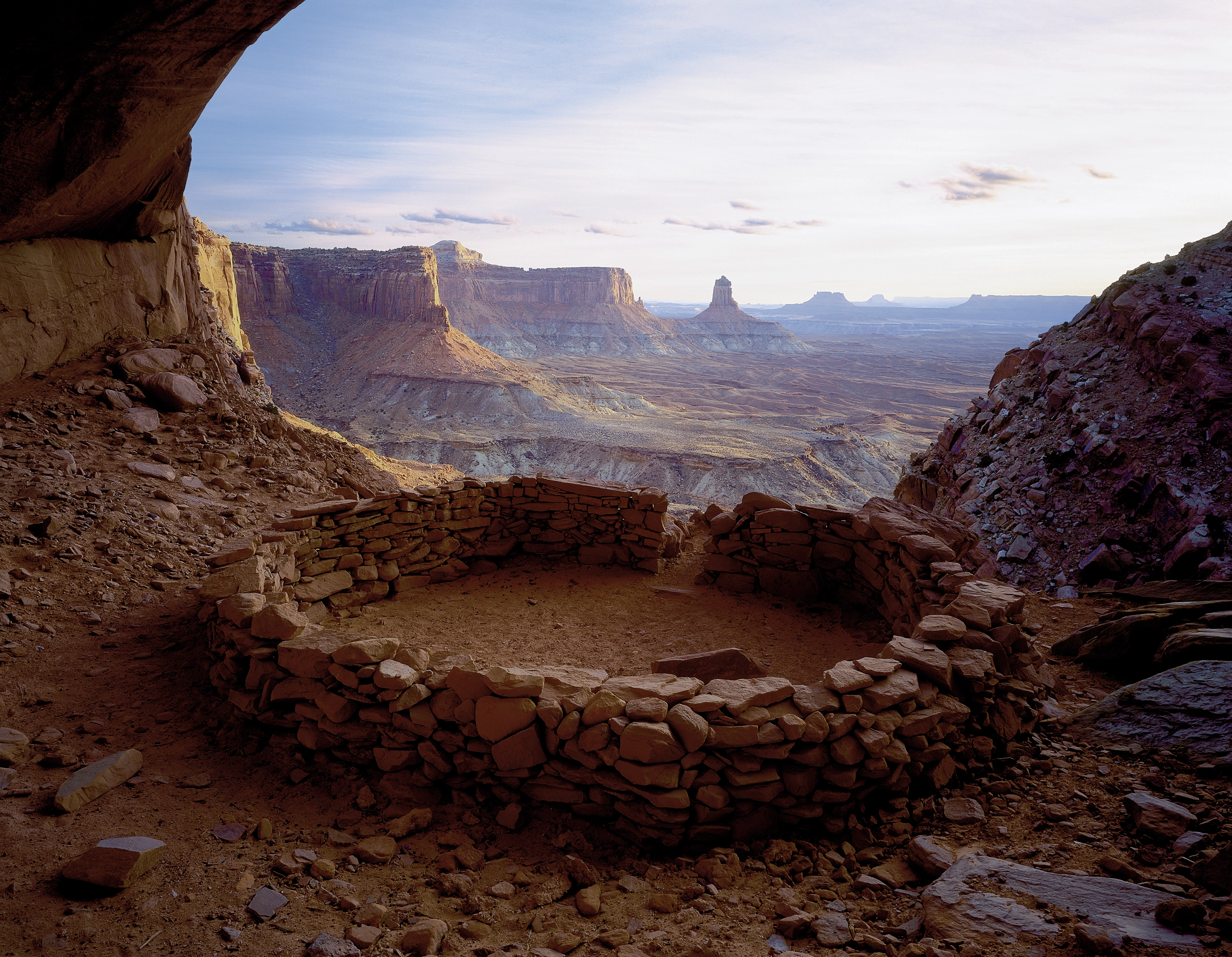 Circular stone ruin or kiva on a rocky mesa, with expansive canyon cliffs visible beyond.