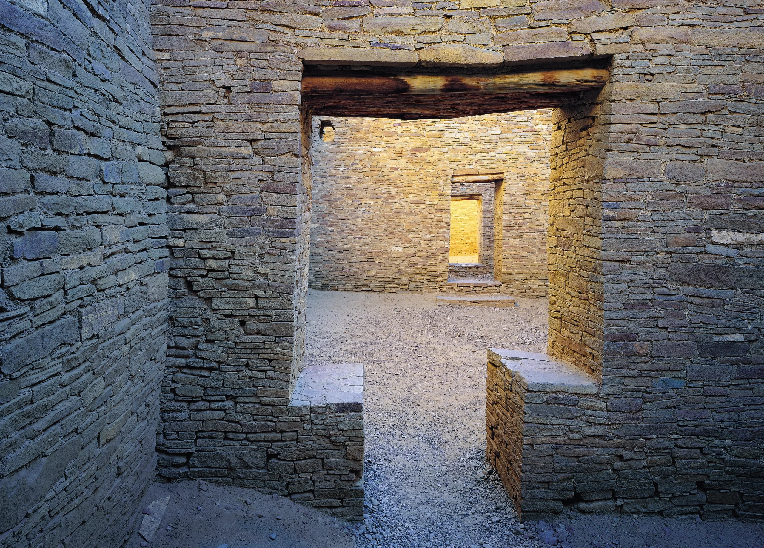 View through a series of rectangular stone doorways into a sunlit courtyard enclosed by masonry walls.