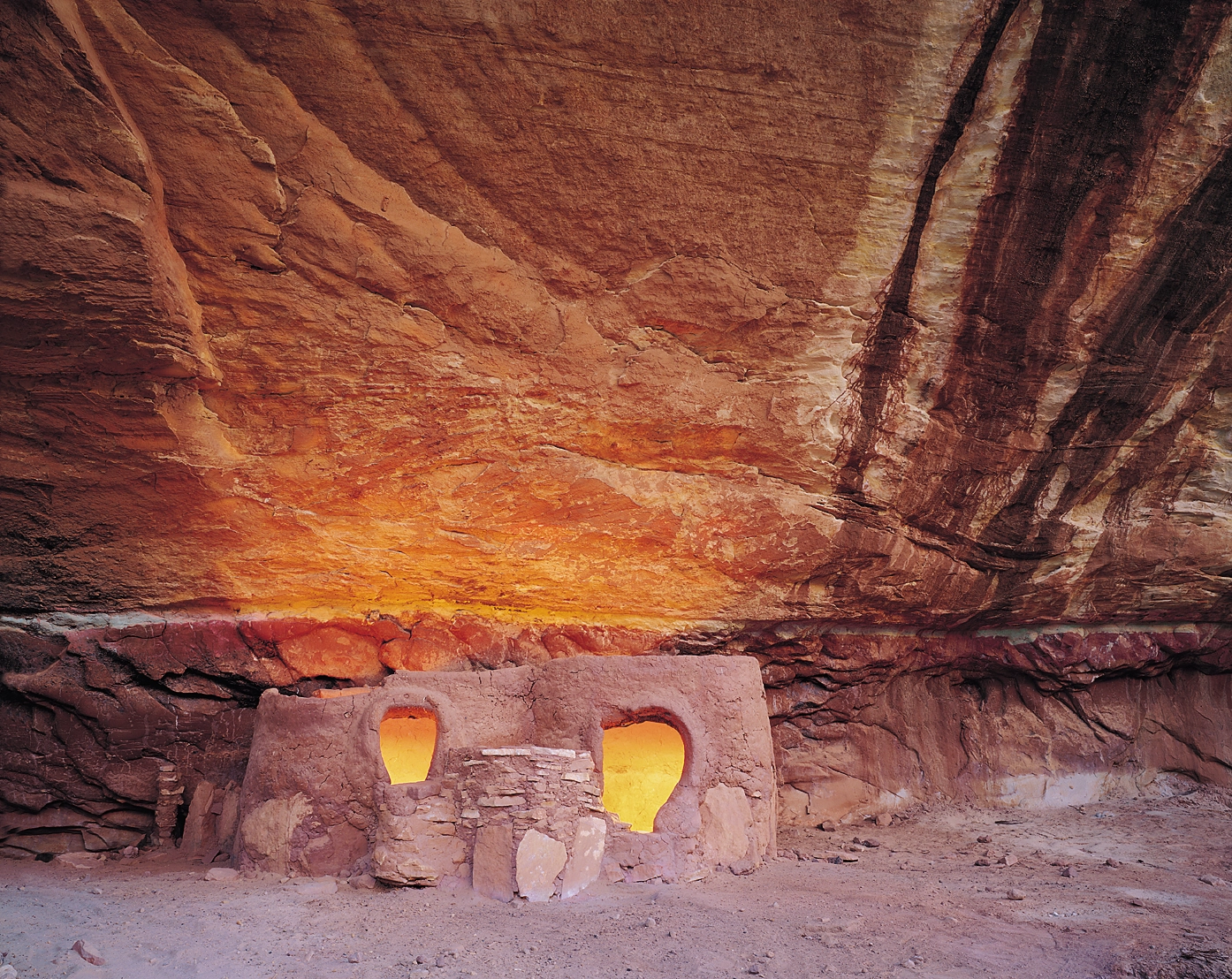 Two small doorways in a stone dwelling tucked beneath a dark red sandstone overhang.