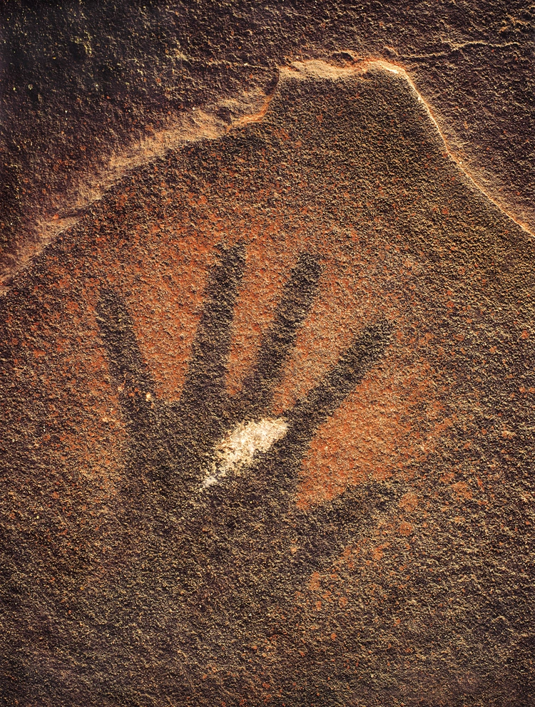 Ochre-colored handprint painted or pressed onto a dark, textured rock surface.